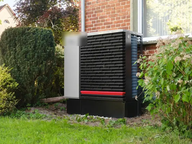 Dark gray heat pump outdoor unit on a lawn next to a house