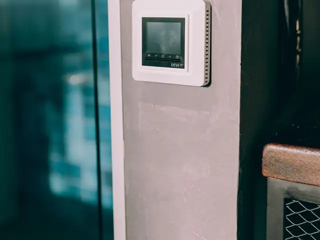 Digital smart thermostat mounted on a wall next to a window
